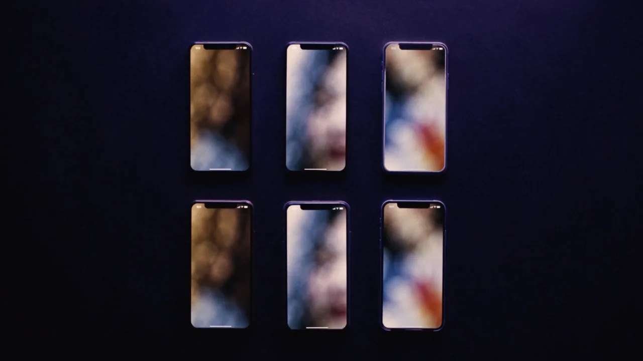 Six téléphones alignés sur une table sombre, écrans allumés, pour comparaison